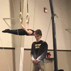 A small boy doing gymnastics along with instructor