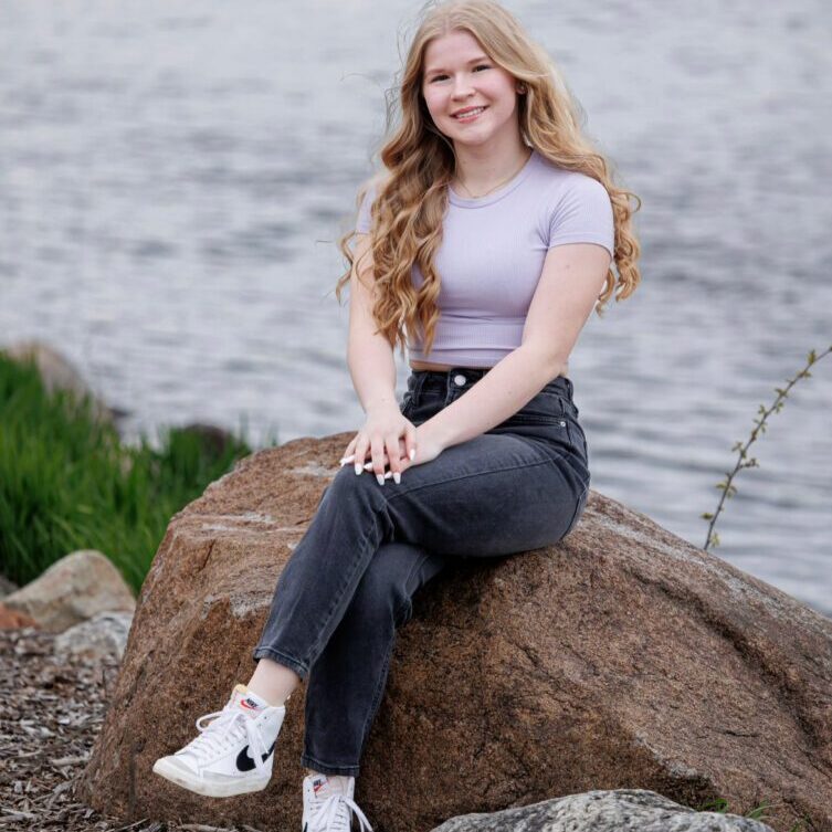 Girl sitting on a rock by water.