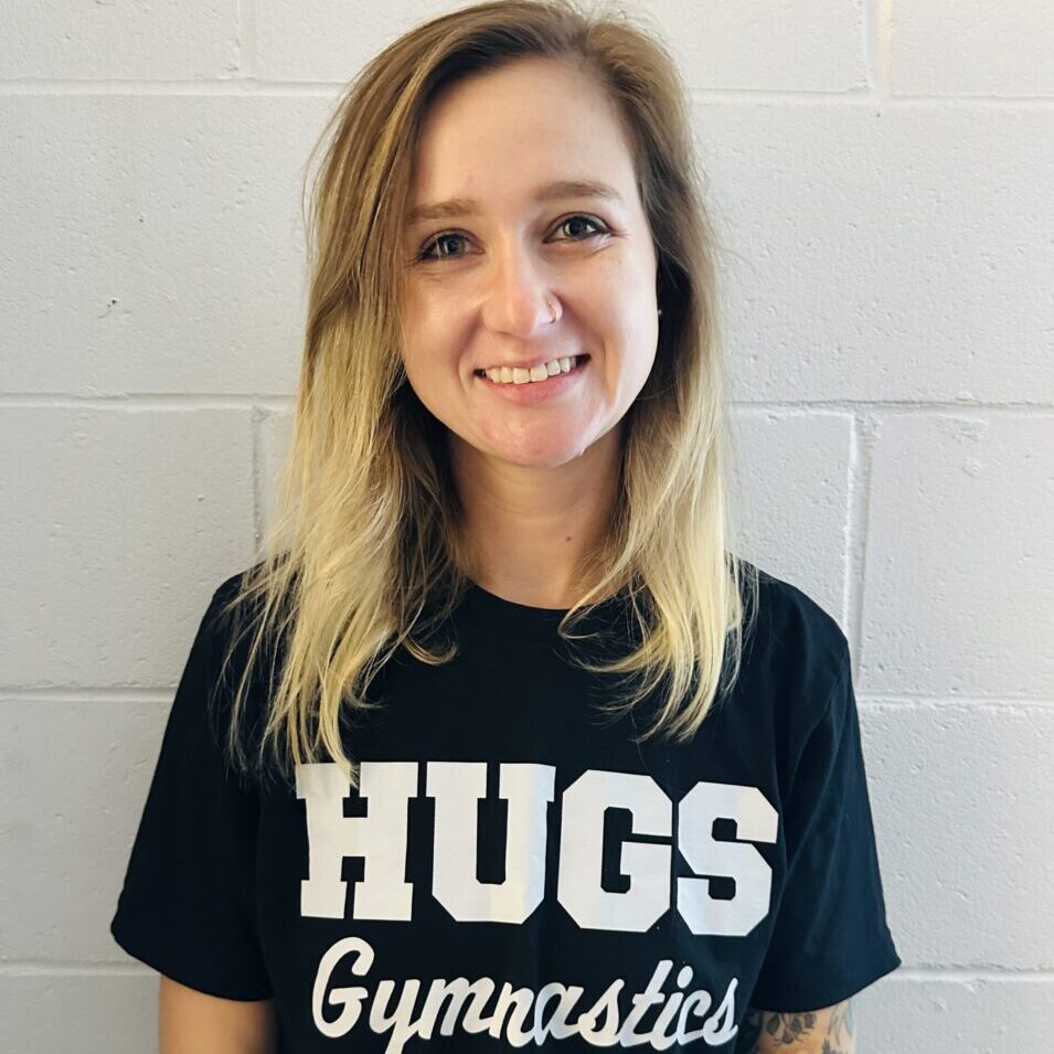 Smiling individual wearing a "HUGS Gymnastics" shirt.